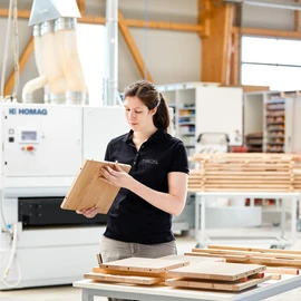 Woman works in carpentry and checks a piece of wood.