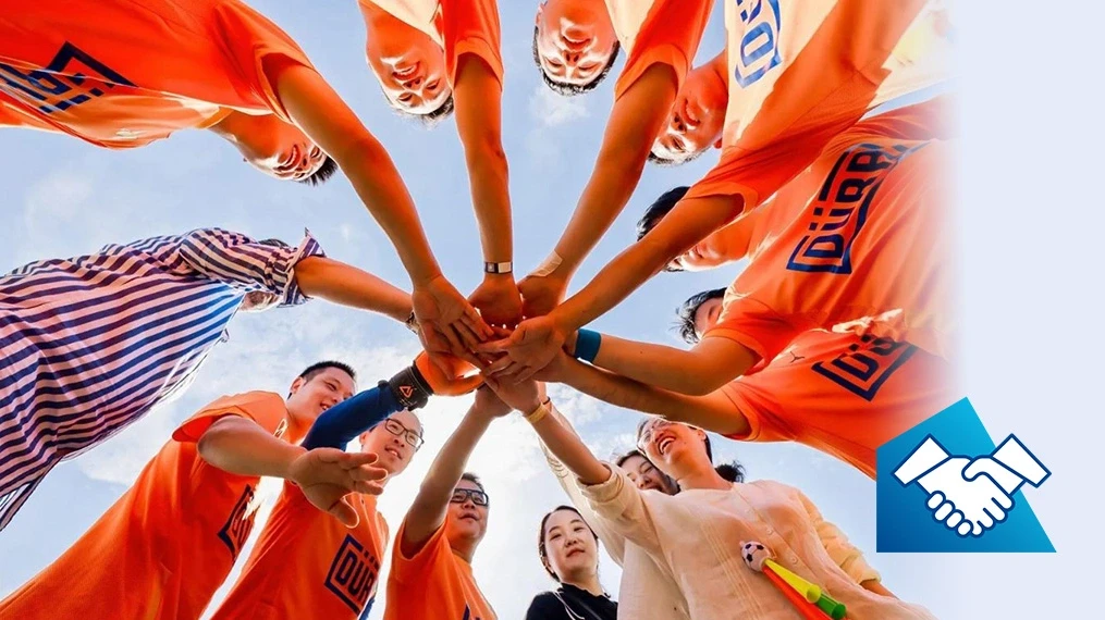 Dürr employees at a sporting event holding their hands in the middle