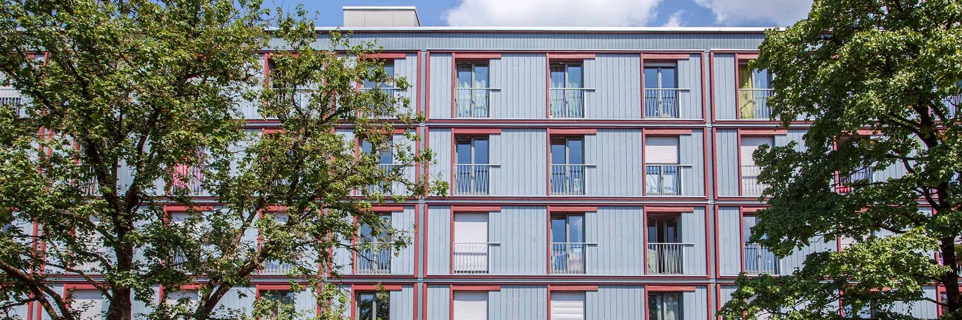 Timber construction facade behind trees.