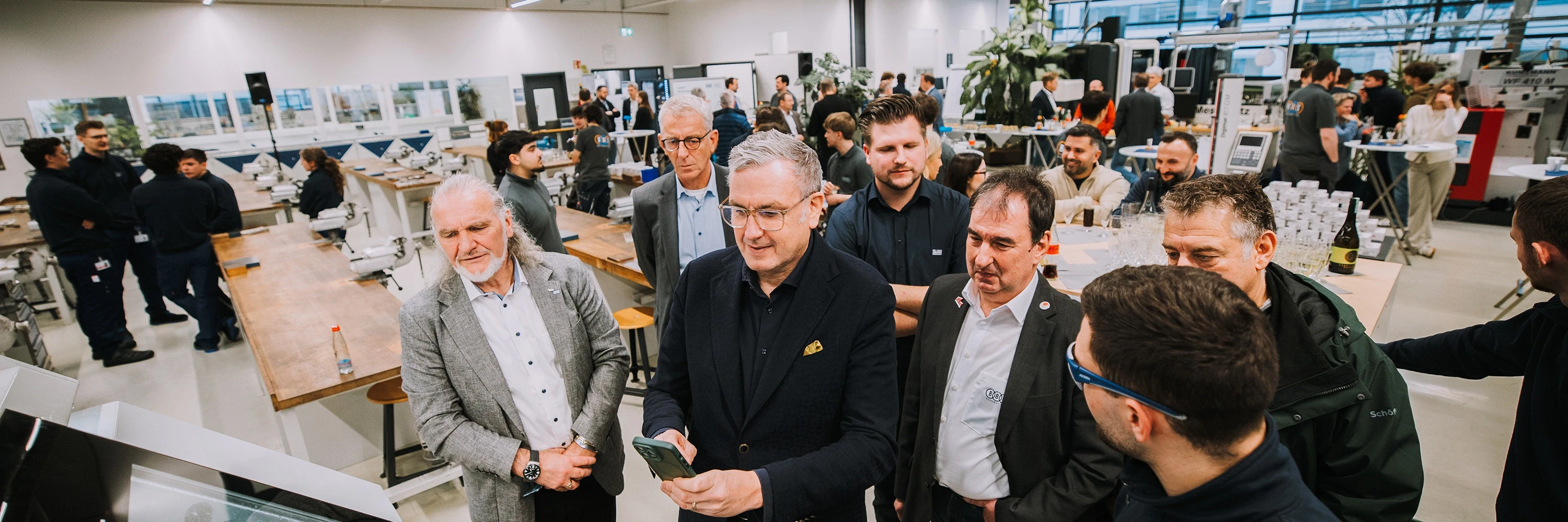Vocational training center 01 Group of people in a modern training center surrounded by workbenches and technical equipment, with others engaged in conversations in the background
