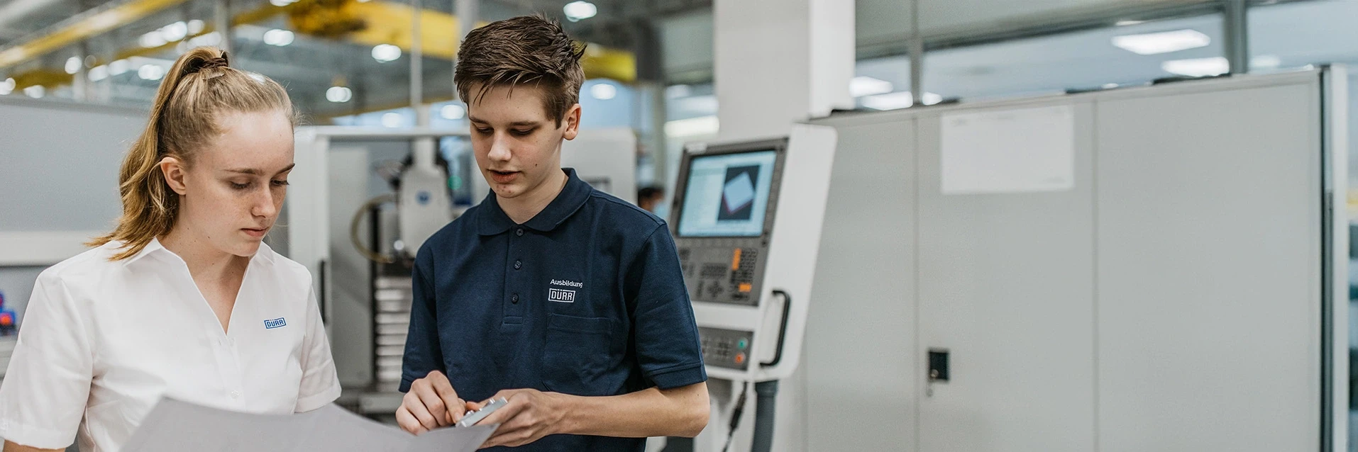 Zwei Auszubildende von Dürr betrachten einen Plan.